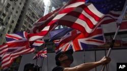 Seorang pedemo mengibarkan bendera AS dan Inggris saat berpawai ke kantor polisi Tsim She Tsui di Hong Kong, 20 Oktober 2019.