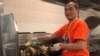 Satriyo Utomo alias Nanang, ketua tim relawan dapur Muktamar IMSA 2019, menggoreng ikan filet di dapur (VOA/Karlina).