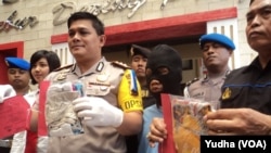 Polisi menujukkan tersangka pedofilia (baju tahanan warna biru--tengah) dan barang bukti sejumlah pakaian anak korban pedofil (Foto: VOA/Yudha)