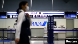 FILE - An employee, wearing protective mask following an outbreak of the coronavirus disease (COVID-19), passes in front of an All Nippon Airways (ANA) counter at the almost empty Kansai International Airport in Osaka, Japan, March 14, 2020. 