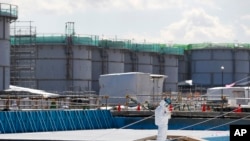 Seorang karyawan dengan pakaian pelindung sedang mencatat di depan pembangkit tenaga nuklir milik Tokyo Electric Power Co. di kota Okuma, prefektur Fukushima, Jepang, 10 Februari 2016. (Foto:dok)