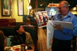 Seorang pria menunjukkan poster wajah calon presiden AS dari Partai Demokrat, Joe Biden, dan pasangannya, Kamala Harris, sementara pengunjung lain menyaksikan laporan hasil pemilu di bar di Taipei, Taiwan, Selasa, 4 November 2020. (Foto: Reuters)