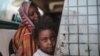 Seorang ibu dan anak perempuannya tengah menunggu bus di Izba, dekat Khartoum, Sudan, 14 Apri 2015. (Foto: dok).