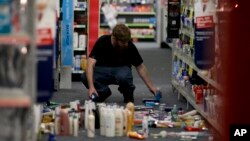 A man picks up fallen goods at a CVS store after an earthquake, March 28, 2014, in La Mirada, California.