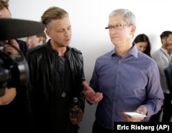 Apple CEO Tim Cook, right, looks at the new iPhone 6s with the members of OneRepublic, in the demo room after Apple event at the Bill Graham Civic Auditorium in San Francisco, Wednesday, Sept. 9, 2015.