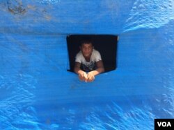 A displaced Sunni teenager looks out of a window cut into plastic blue sheeting covering his new home in the Baharka camp on the outskirts of Irbil, in the Kurdistan region of Iraq, Aug 5, 2015. (VOA / S.Behn)