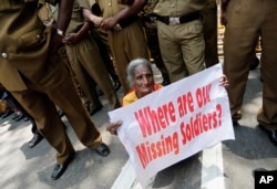 FILE - A Sri Lankan ethnic Tamil woman supporting the Dead and Missing Person’s Parents Front holds a placard as police officers stand guard during a protest in Colombo, Sri Lanka, Aug. 30, 2013.