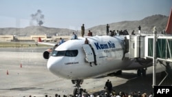 Afghan people climb atop a plane as they wait at the Kabul airport in Kabul on August 16, 2021, after a stunningly swift end to Afghanistan's 20-year war, as thousands of people mobbed the city's airport trying to flee the group's feared hardline brand of