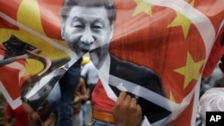 A Karni Sena supporter tears a banner featuring Chinese President Xi Jinping and shout slogans during a protest against China in Ahmedabad, India, Wednesday, June 24, 2020. 