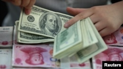 Seorang pegawai bank di Huaibei, provinsi Anhui, China sedang menghitung uang kertas dengan nominal 100 dolar Amerika di atas lembaran mata uang kertas dengan nominal 100 yuan China (Foto: dok).