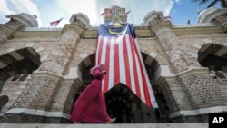 Seorang warga muslim berjalan melewati bendera Malaysia di depan gedung Sultan Abdul Samad, Independence Square, Kuala Lumpur, Malaysia (Foto: dok).