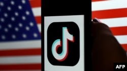 Logo aplikacije TikTok na ekranu ajfona, ispred zastave SAD. (Ilustracija: Olivier DOULIERY / AFP)