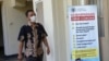 Seorang staf UGM melintas di depan poster terkait Virus Corona di kampus tersebut. (Foto:VOA/ Nurhadi)
