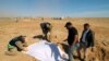 FILE - Iraqi members of the Civil Defense cover the bones from an unearthed mass grave of Kurds in west of the city of Samawah, Iraq, April 14, 2019.