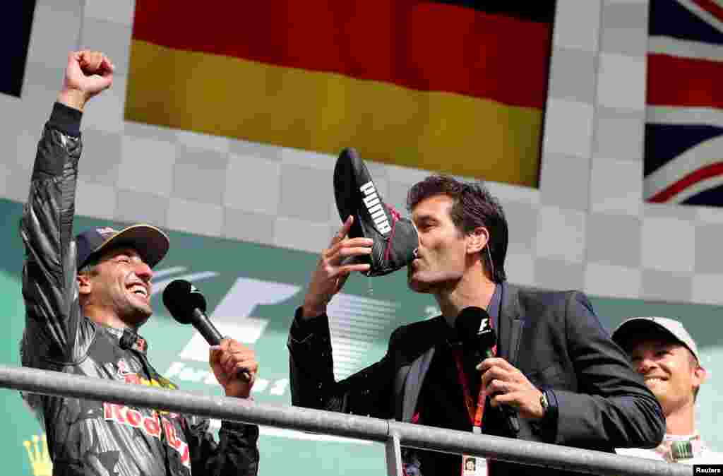 Former Formula One driver Mark Webber of Australia drinks champagne from the shoe of Red Bull's Daniel Ricciardo of Australia (L) while Mercedes' Nico Rosberg of Germany (R) looks on after the Belgian F1 Grand Prix.