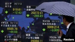Seorang pejalan kaki yang memegang payung melihat papan elektronik indeks pasar saham berbagai negara di Tokyo, Jepang, 6 Juli 2015. (Foto: Reuters)