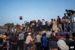 Warga Palestina menyerbu truk berisi bantuan kemanusiaan yang dibawa melalui dermaga baru yang dibangun AS, di Jalur Gaza tengah, Sabtu, 18 Mei 2024. (Foto: AP)