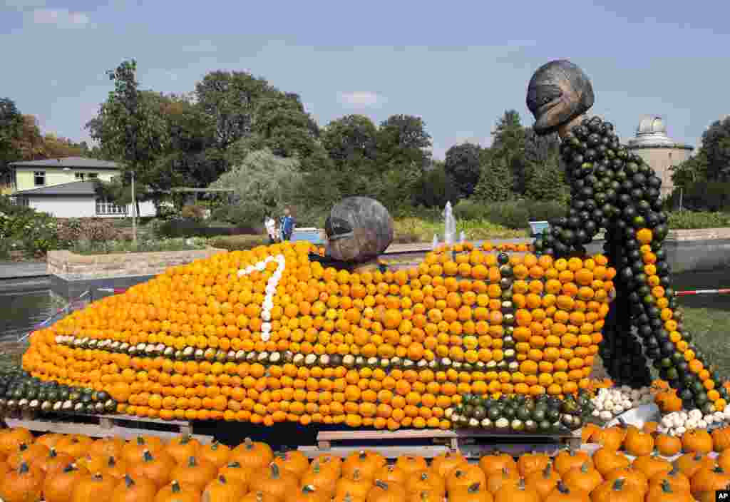 Visitors walk behind a sculpture of bobsledders during preparations of the autumn pumpkins exhibition 'Sports' at the horticultural exhibition 'ega' in Erfurt, central Germany.