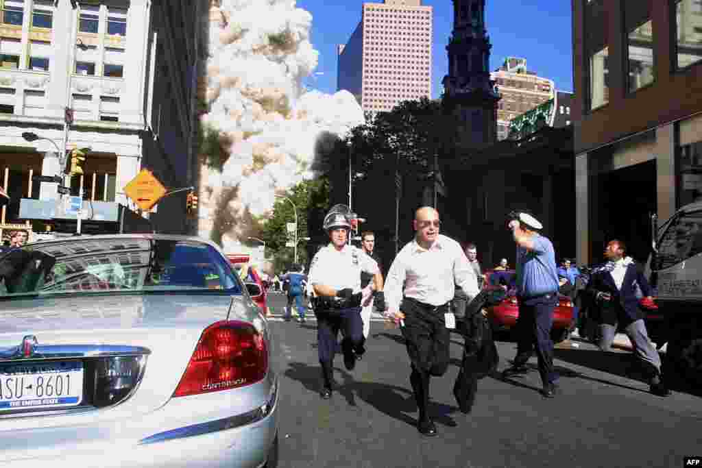 (FILE) Police and pedestrians run for cover during the first collapse of the World Trade Center Tower after the landmark skyscrapers were struck by two hijacked airplanes 11 September 2001 in New York . AFP PHOTO/Doug KANTER (Photo by DOUG KANTER / AFP)