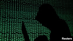 Seorang berpenutup kepala mengangkat komputer laptop saat kode siber diproyeksikan ke arahnya pada sebuah gambar ilustrasi yang diambil pada tanggal 13 Mei 2017 (foto: REUTERS/Kacper Pempel/Ilustrasi)